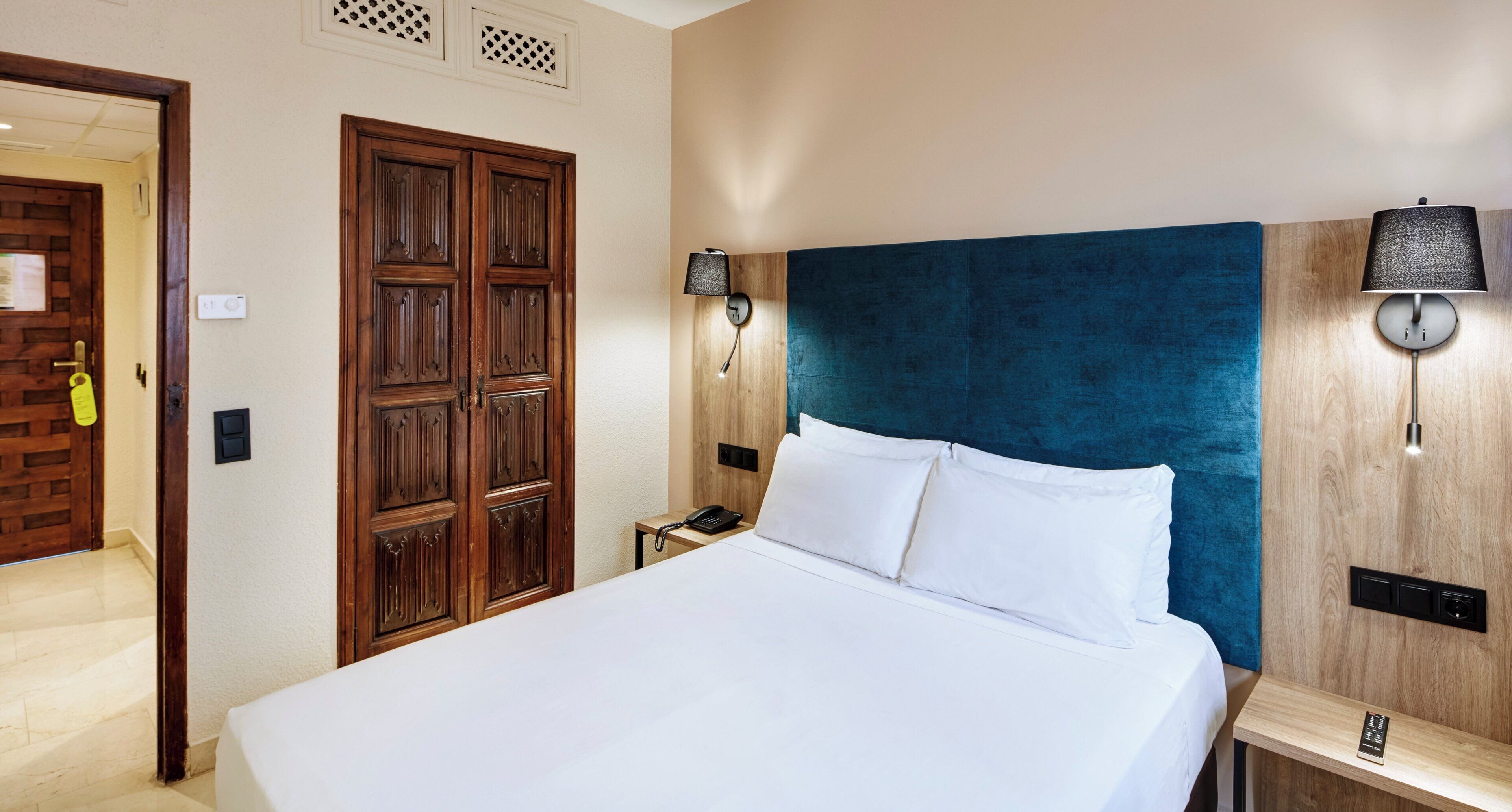 A hotel room with a large bed, wooden wardrobe, two bedside lamps, and a bedside phone.