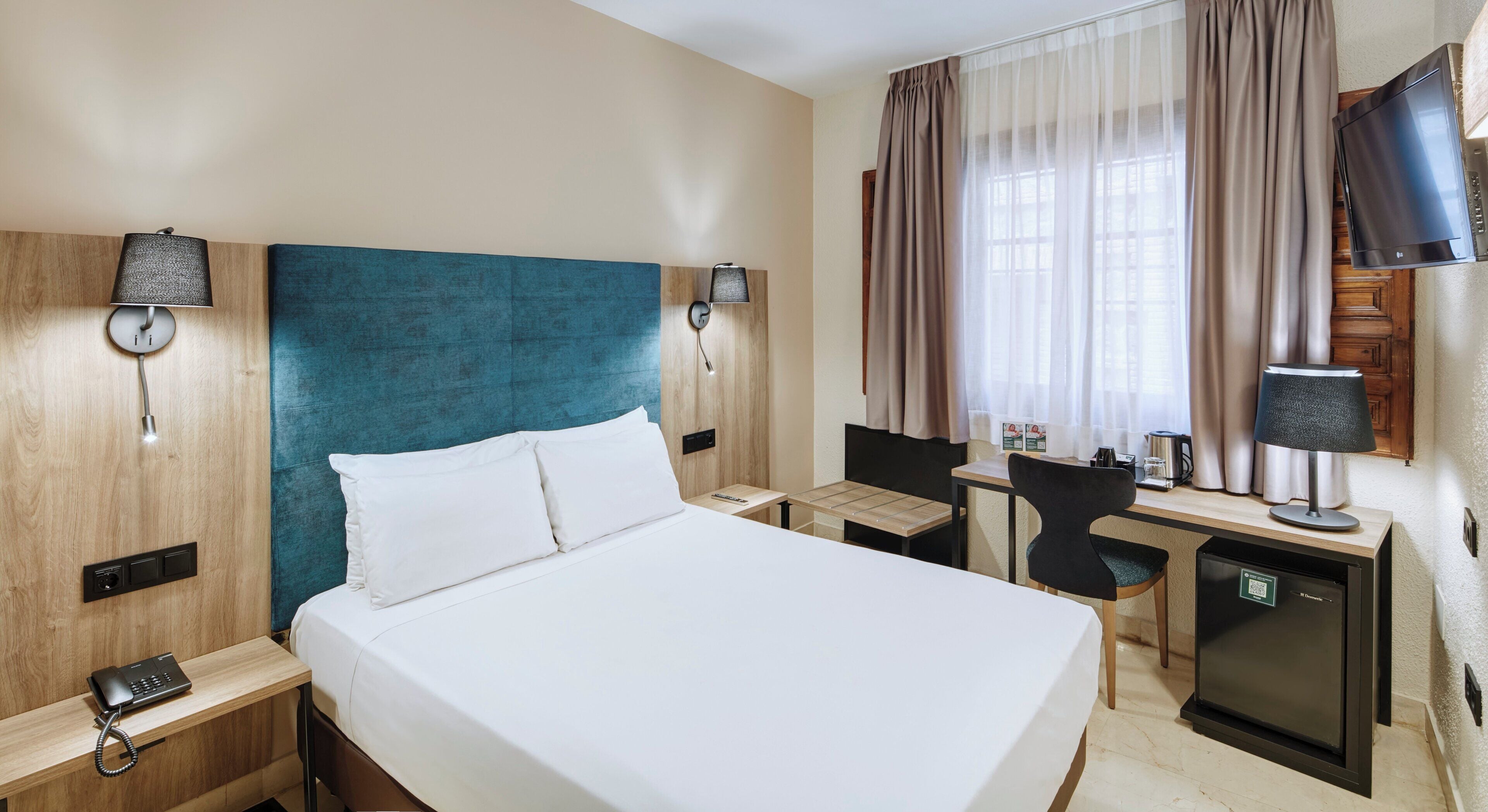 Ein Hotelzimmer mit einem großen Bett, einem Schreibtisch mit Stuhl, einer kleinen Küchenzeile und einem Fernseher.