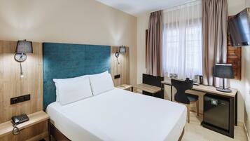Ein Hotelzimmer mit einem großen Bett, einem Schreibtisch mit Stuhl, einer kleinen Küchenzeile und einem Fernseher.