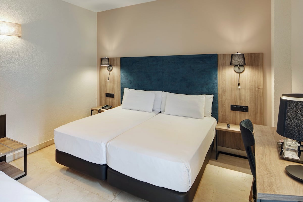 Une chambre d’hôtel avec un lit double, des tables de chevet, un bureau avec une chaise et deux lampes fixées au mur.
