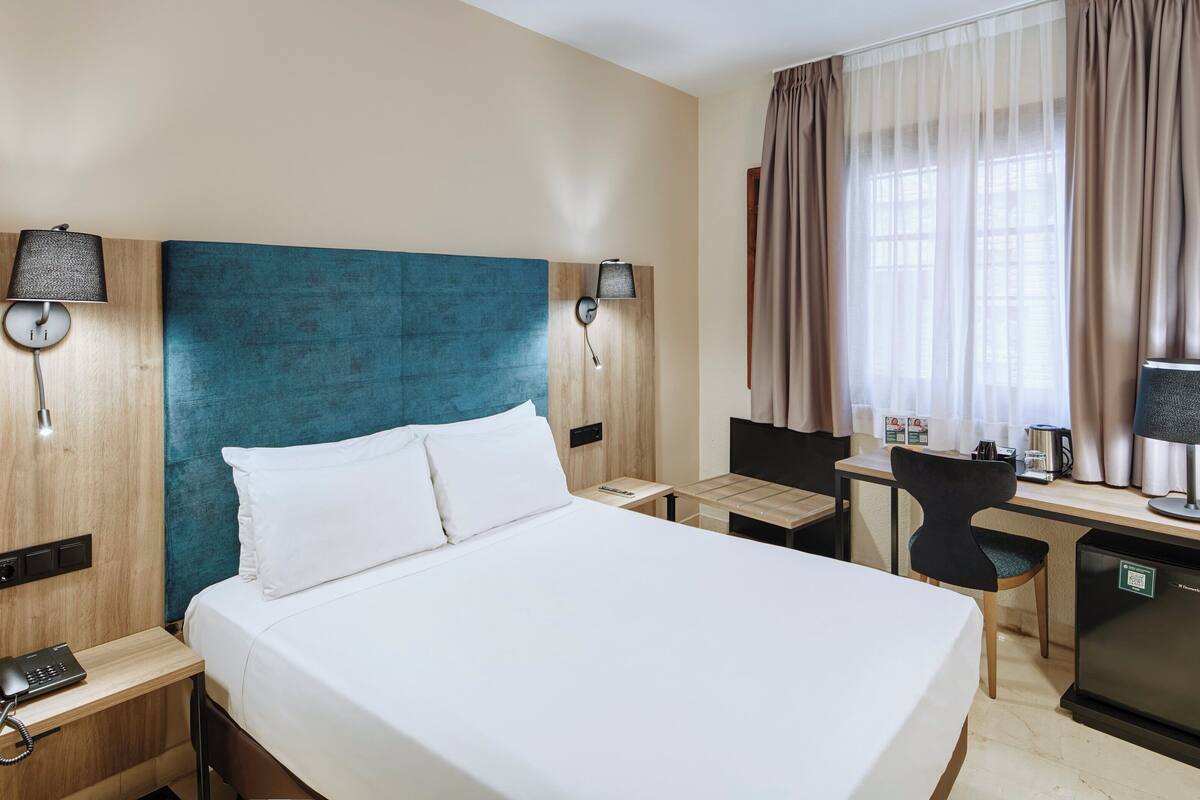Une chambre d’hôtel avec un grand lit, un bureau avec une chaise, une petite kitchenette et un téléviseur.