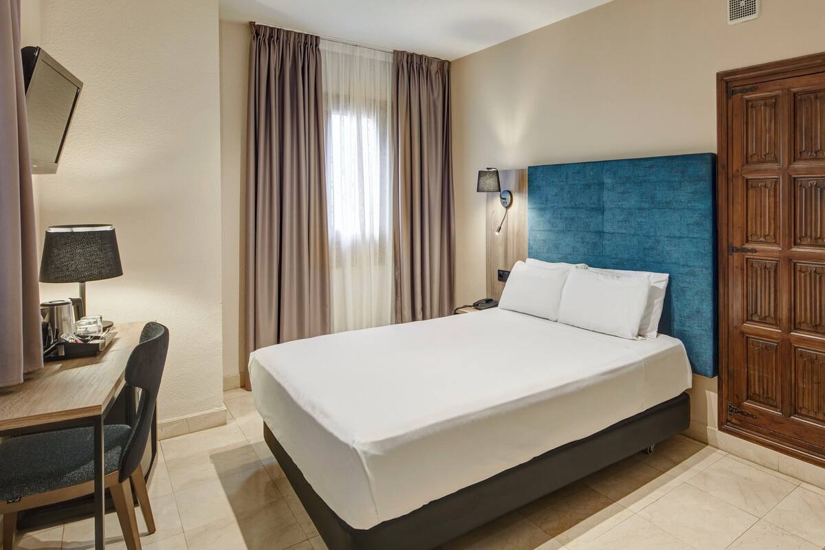 Ein Hotelzimmer mit Bett, Schreibtisch mit Lampe und Kleiderschrank.