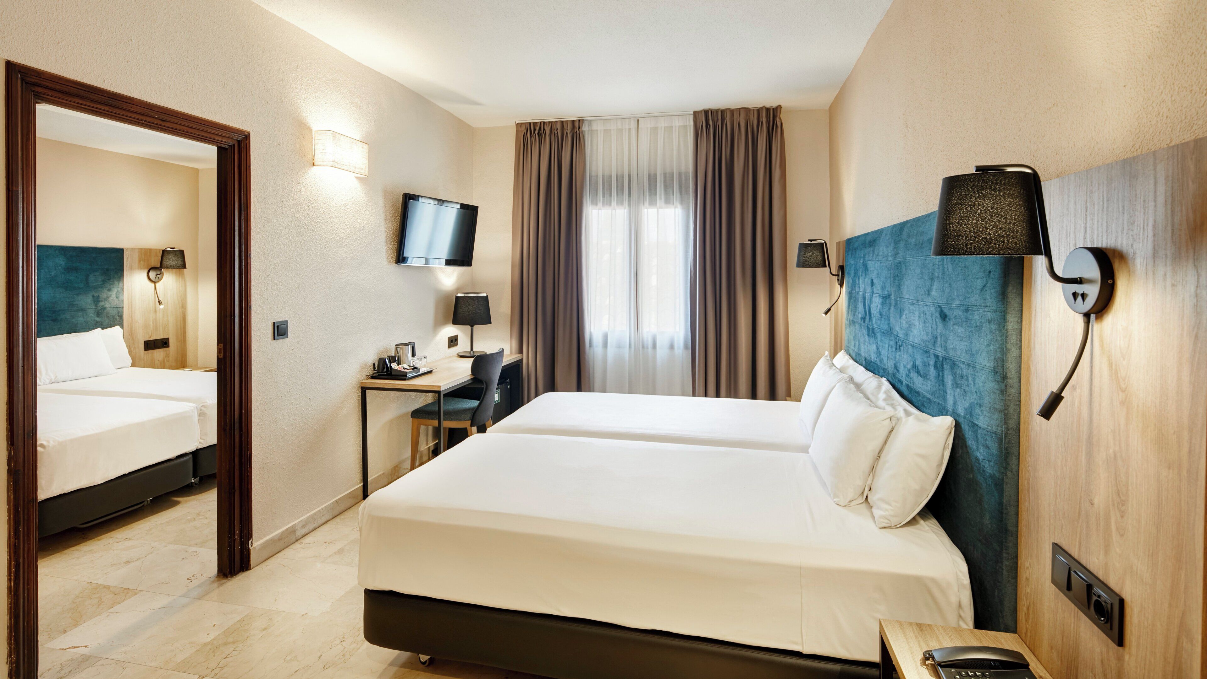 Habitación de hotel con dos camas, un escritorio, una silla, un televisor y un espejo.