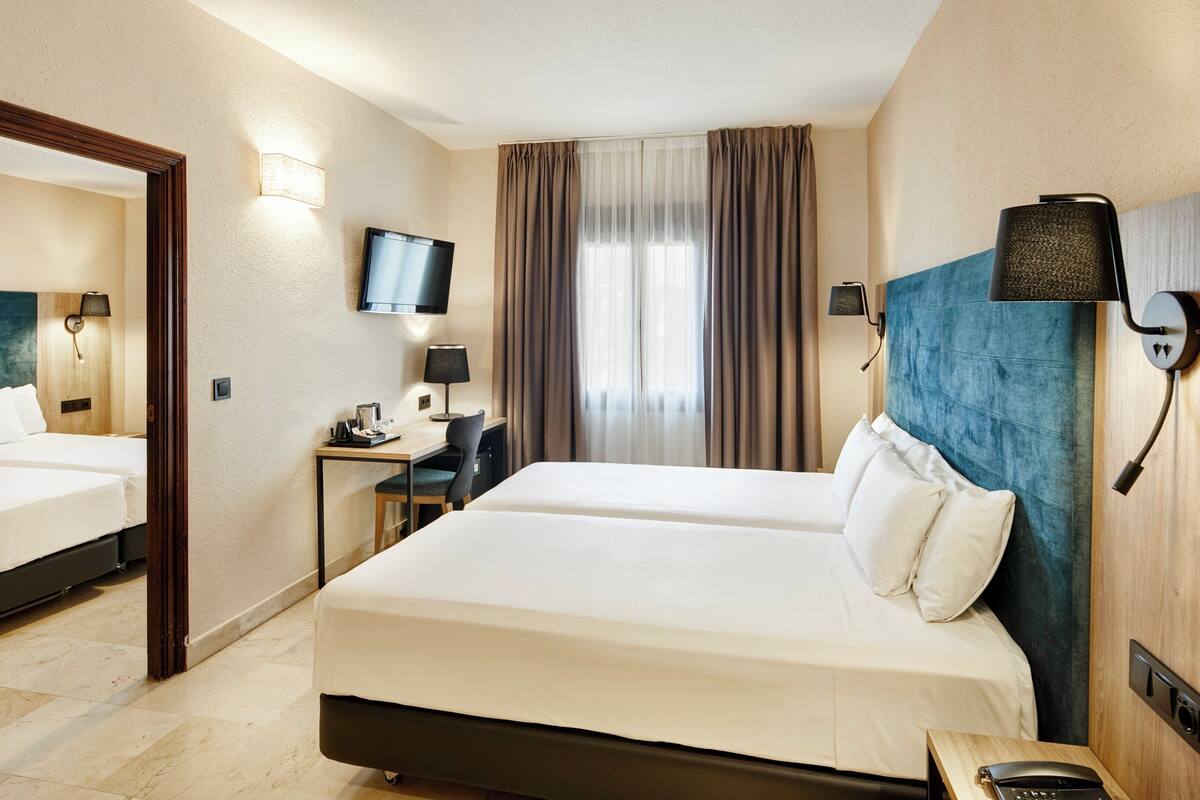 Ein Hotelzimmer mit zwei Betten, einem Schreibtisch, einem Stuhl, einem Fernseher und einem Spiegel.