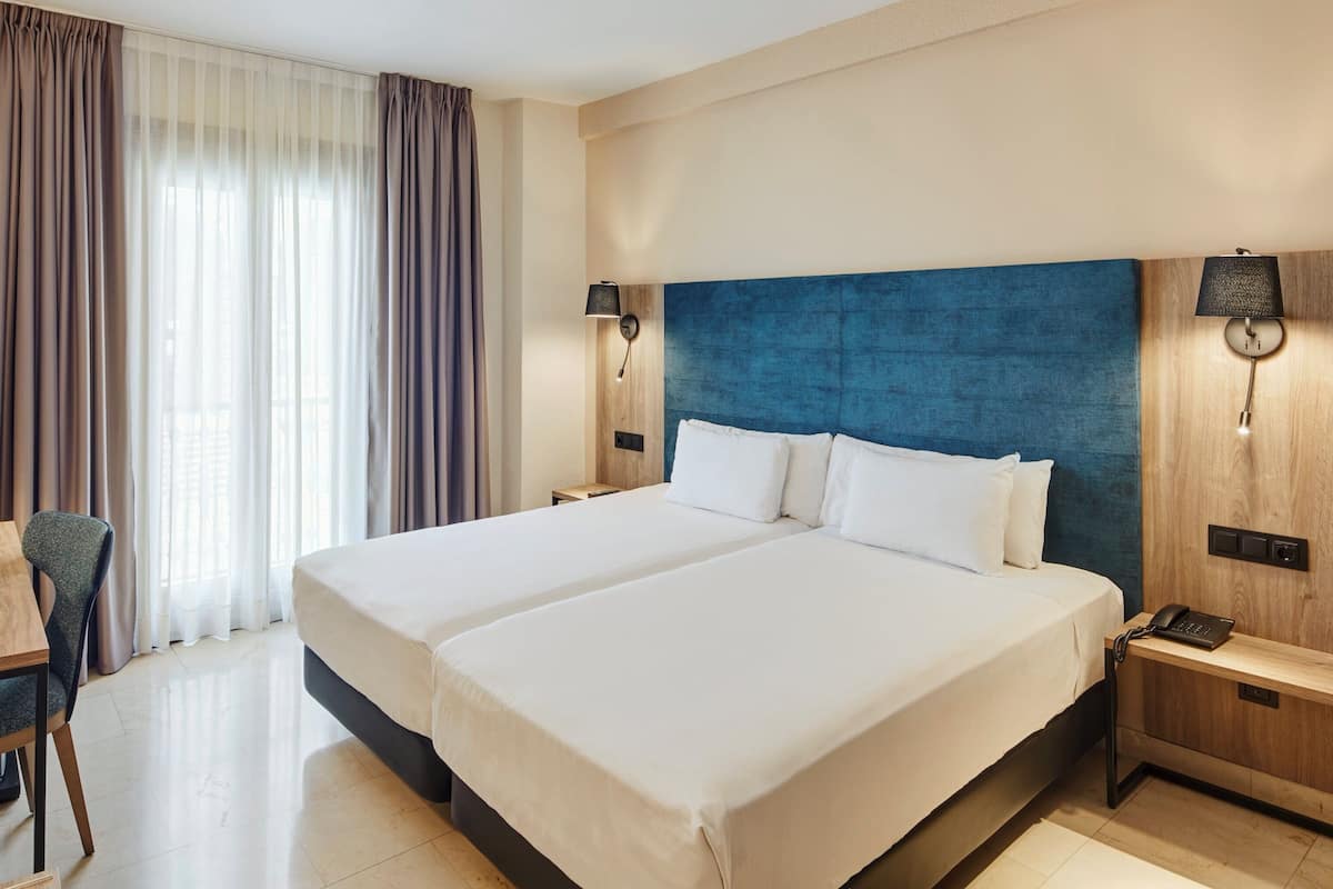Ein Hotelzimmer mit einem großen Bett, einem Schreibtisch mit Stuhl, einem Fernseher und einer Lampe.