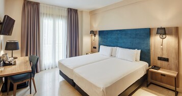Habitación de hotel con una cama grande, un escritorio con silla, un televisor y una lámpara.