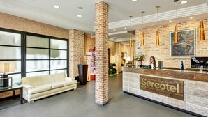 A hotel lobby with a reception desk, a sofa, a large window, and a brick column. - Hotel Sercotel Alfonso VI (Toledo)