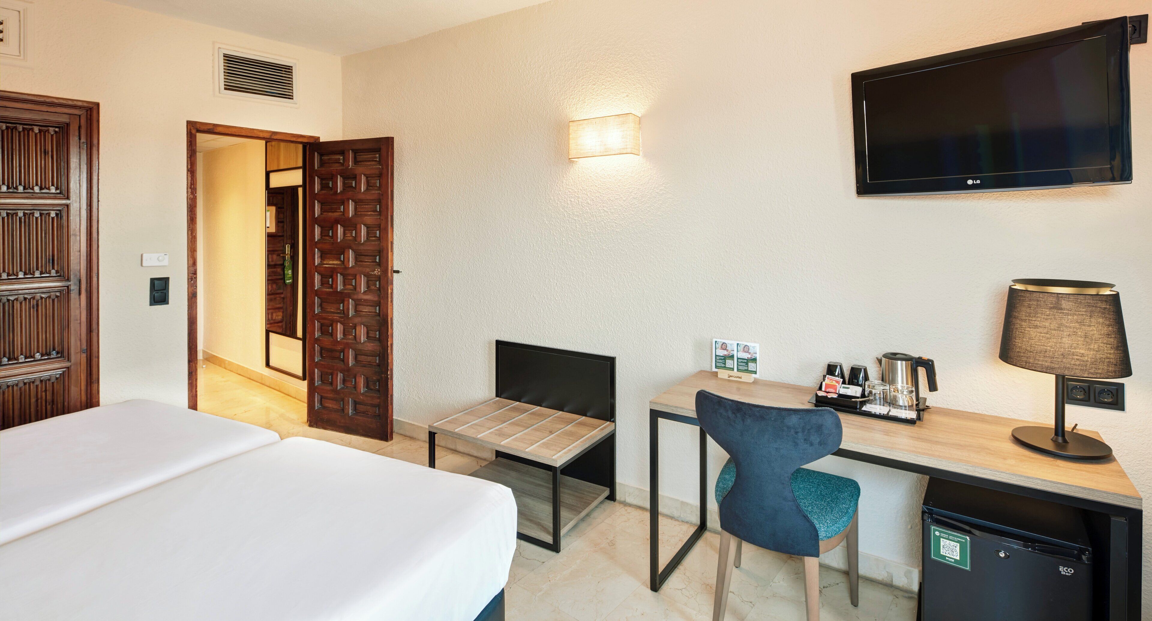 Una habitación de hotel con cama, escritorio, silla, televisor y cafetera.