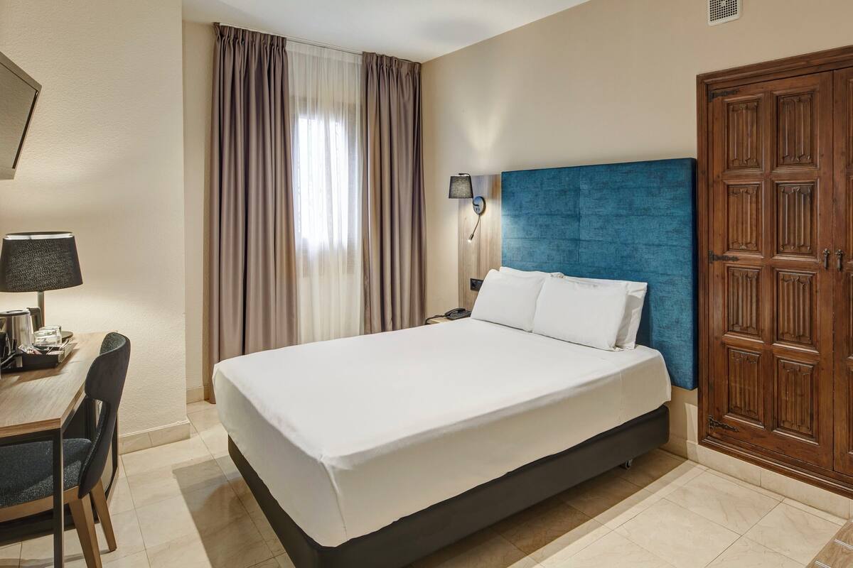 Une chambre d’hôtel avec un lit, un bureau doté d’une lampe et une armoire.