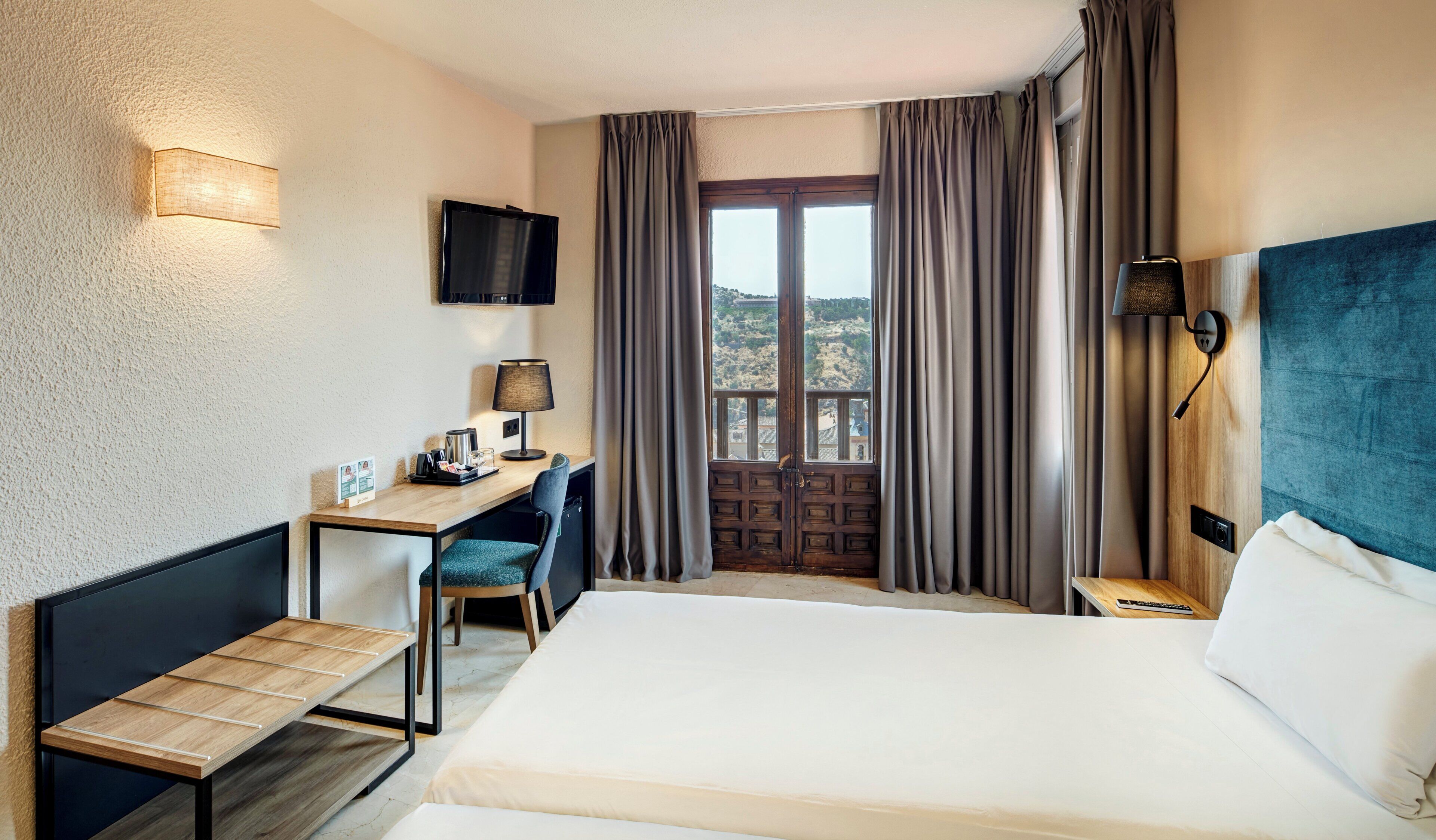 Habitación de hotel con cama, escritorio, silla, lámpara y televisor en la pared.