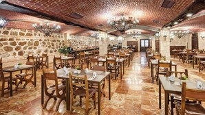 A spacious restaurant with brick walls and stone accents, featuring numerous wooden tables and chairs, and a central chandelier. - Hotel Sercotel Alfonso VI (Toledo)