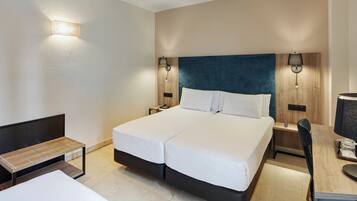 Habitación de hotel con cama doble, mesitas de noche, escritorio con silla y dos lámparas de pared.