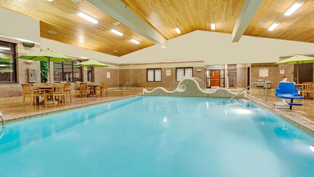 An indoor swimming pool with wooden ceiling, green umbrellas, and wooden chairs around the pool. - Days Inn by Wyndham Cheyenne (Cheyenne)