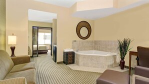 A hotel room with a large bed, a sitting area with a sofa and armchairs, a bathroom with a bathtub, and a mirror on the wall. - Days Inn by Wyndham Cheyenne (Cheyenne)