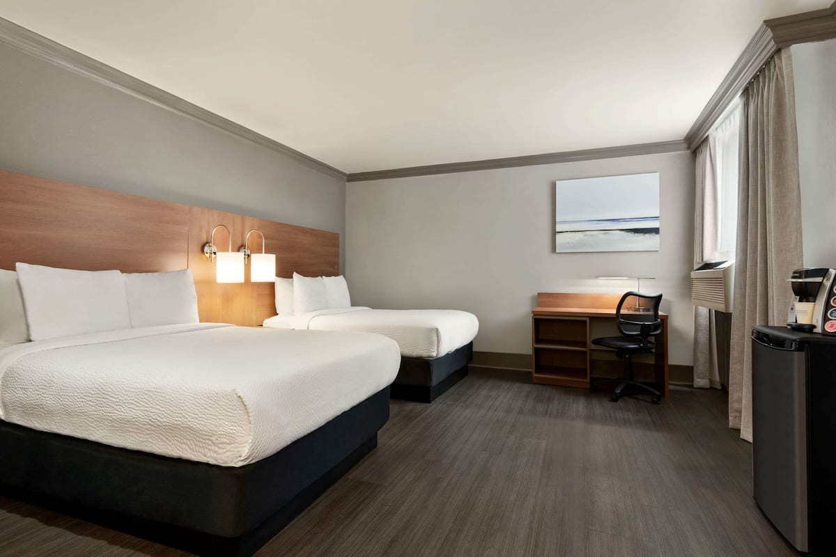 A hotel room with two beds, a desk, a chair, a refrigerator, and a window with curtains.