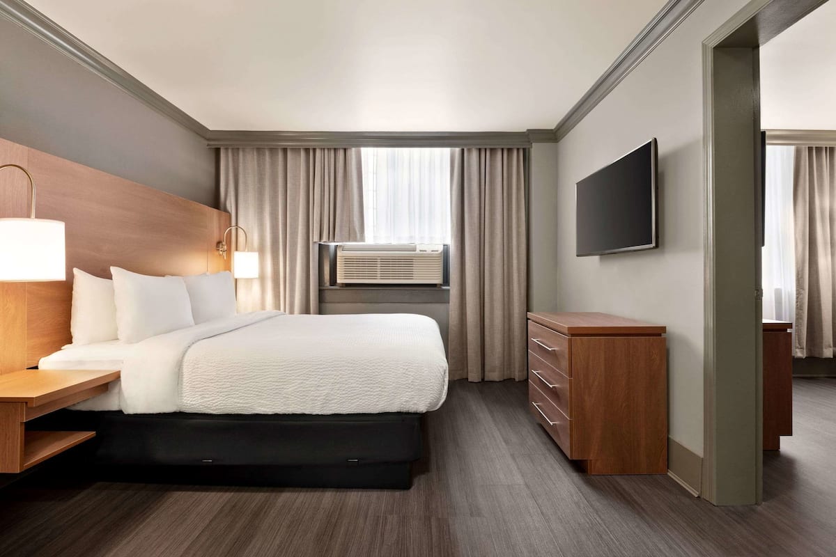 A hotel room with a bed, bedside tables, a TV, a dresser, and an air conditioning unit.