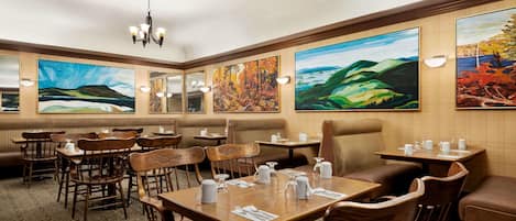 Un restaurante con mesas y sillas de madera, grandes cuadros en las paredes y un candelabro.