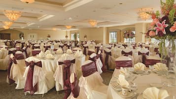 A banquet hall with round tables set for a formal event, featuring white tablecloths and purple sashes.