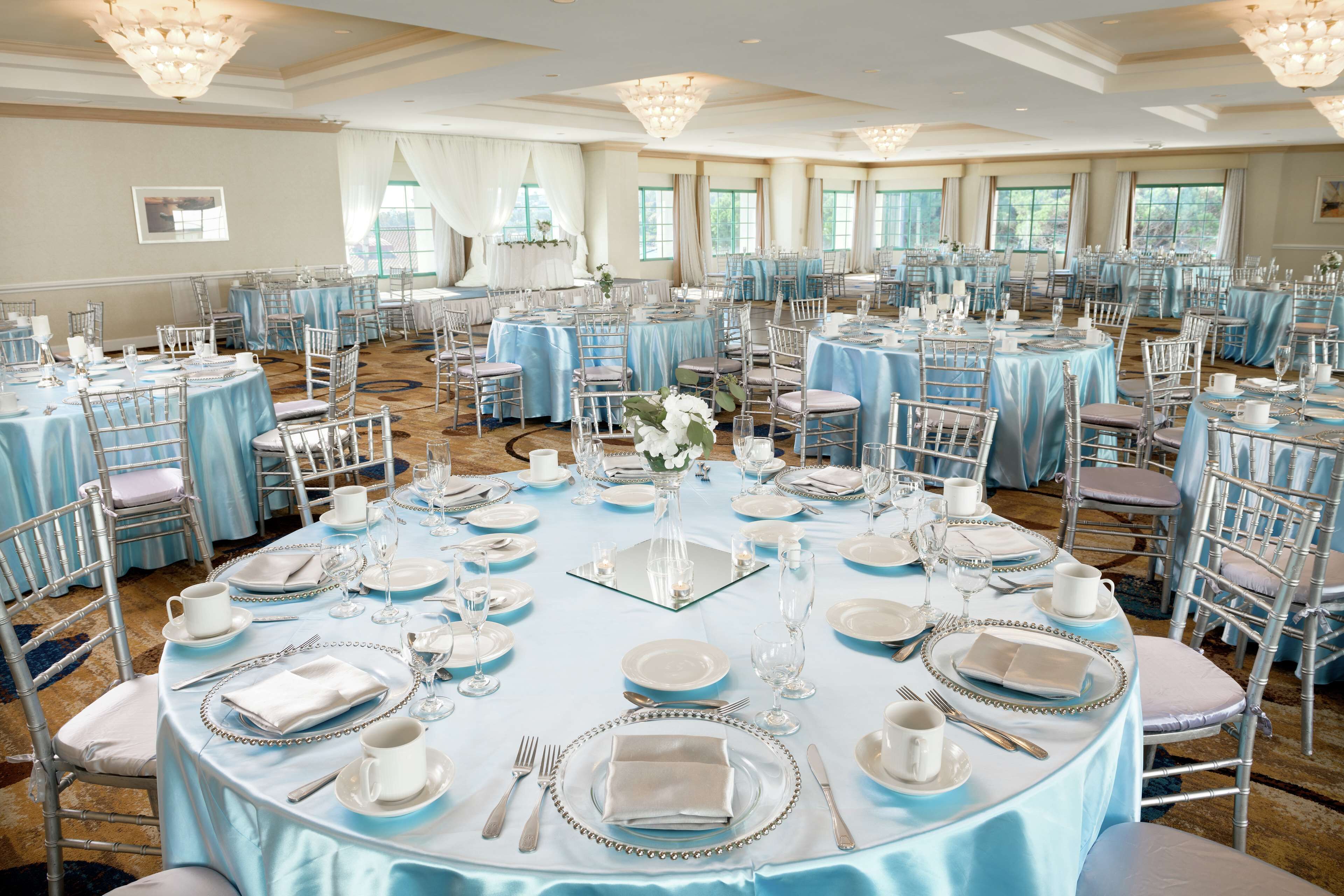 Une salle de banquet avec des tables rondes dressées pour un événement formel, agrémentée de nappes bleues et de chaises blanches.