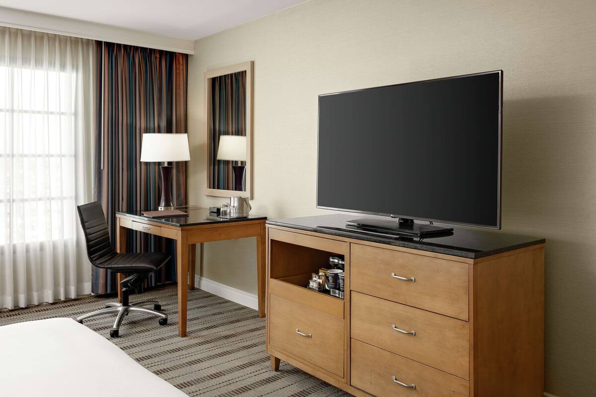 Une chambre d’hôtel comprenant un lit, un bureau avec une chaise, une télévision, une lampe et une armoire.