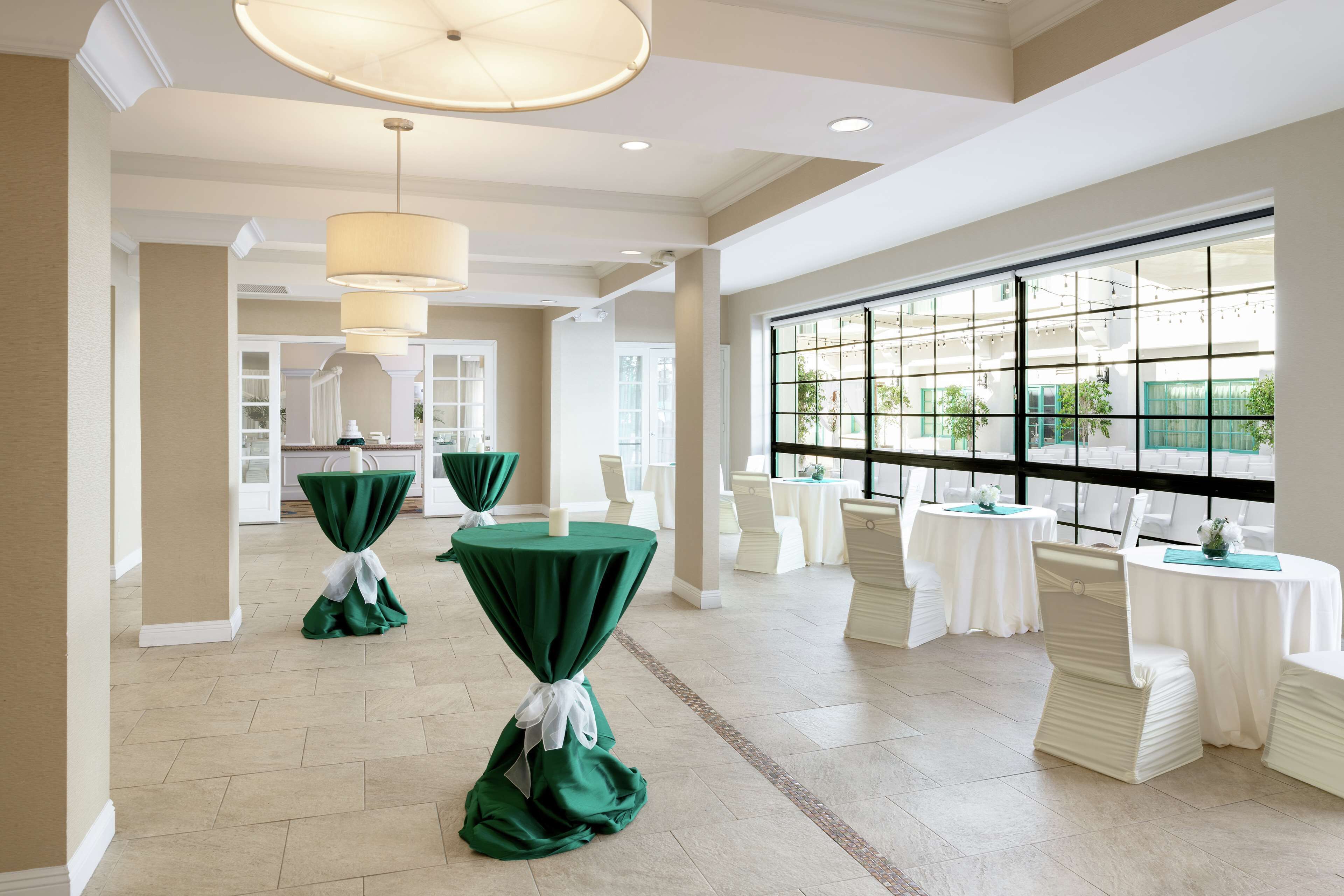 A spacious hall with multiple tables and chairs, large windows, and a high ceiling with pendant lighting.