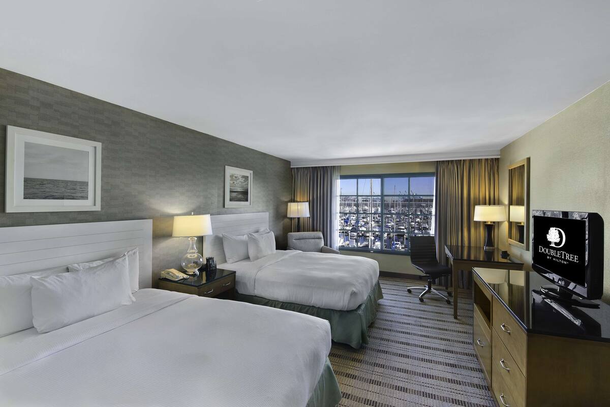 Une chambre d’hôtel avec deux lits, un bureau avec une télévision, une chaise et une vue sur la ville.