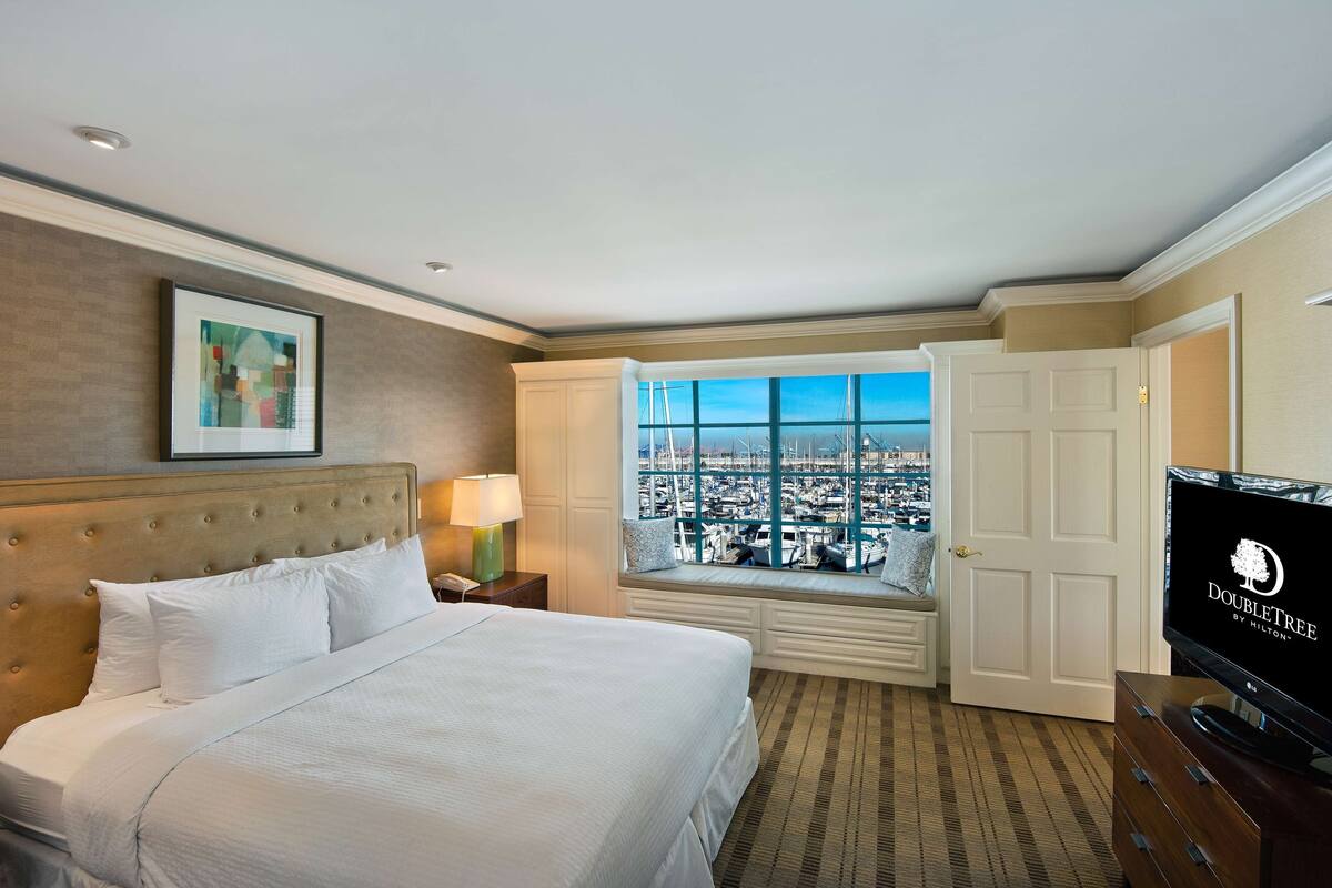 Une chambre d’hôtel avec un grand lit, une télévision, une fenêtre donnant sur la ville et une porte.