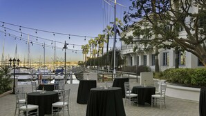 An outdoor dining area with tables and chairs, overlooking a marina with boats. - DoubleTree by Hilton San Pedro - Port of Los Angeles (San Pedro)