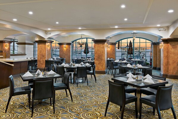 A restaurant with tables set for dining, featuring a patterned carpet and arched windows.