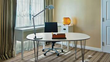Una habitación de hotel con una mesa redonda, una silla, un escritorio, una lámpara y un florero.