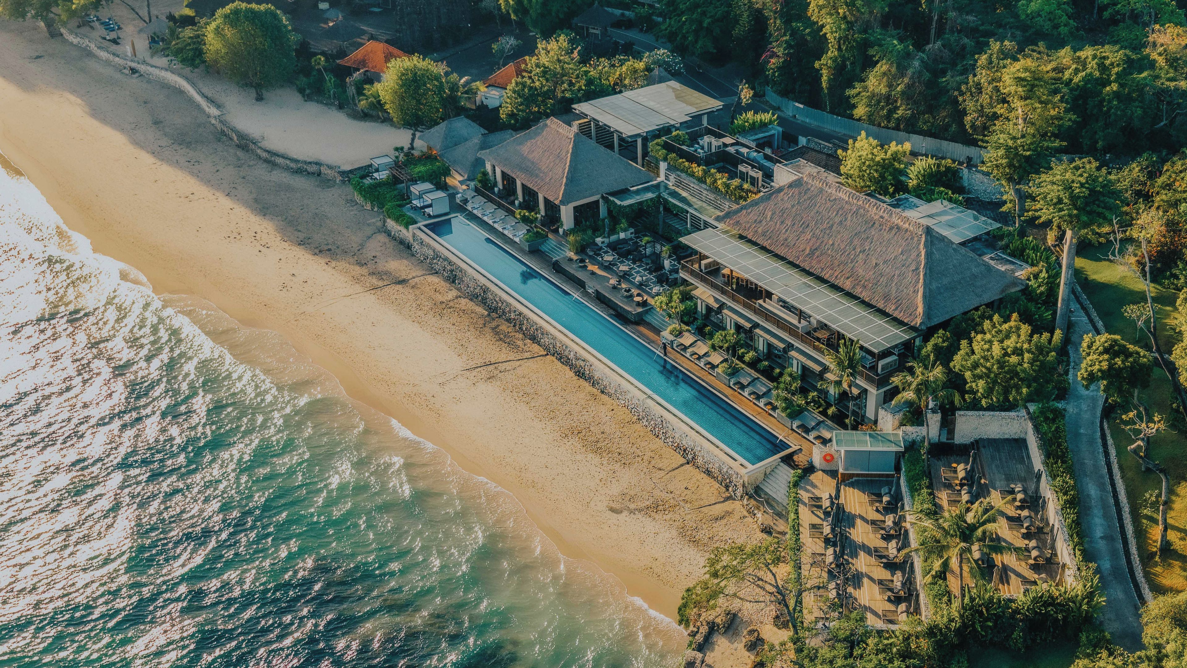 An aerial view of a beachfront property with a swimming pool, multiple buildings, and lush greenery.