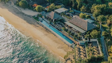 An aerial view of a beachfront property with a swimming pool, multiple buildings, and lush greenery.