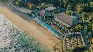 An aerial view of a beachfront property with a swimming pool, multiple buildings, and lush greenery.