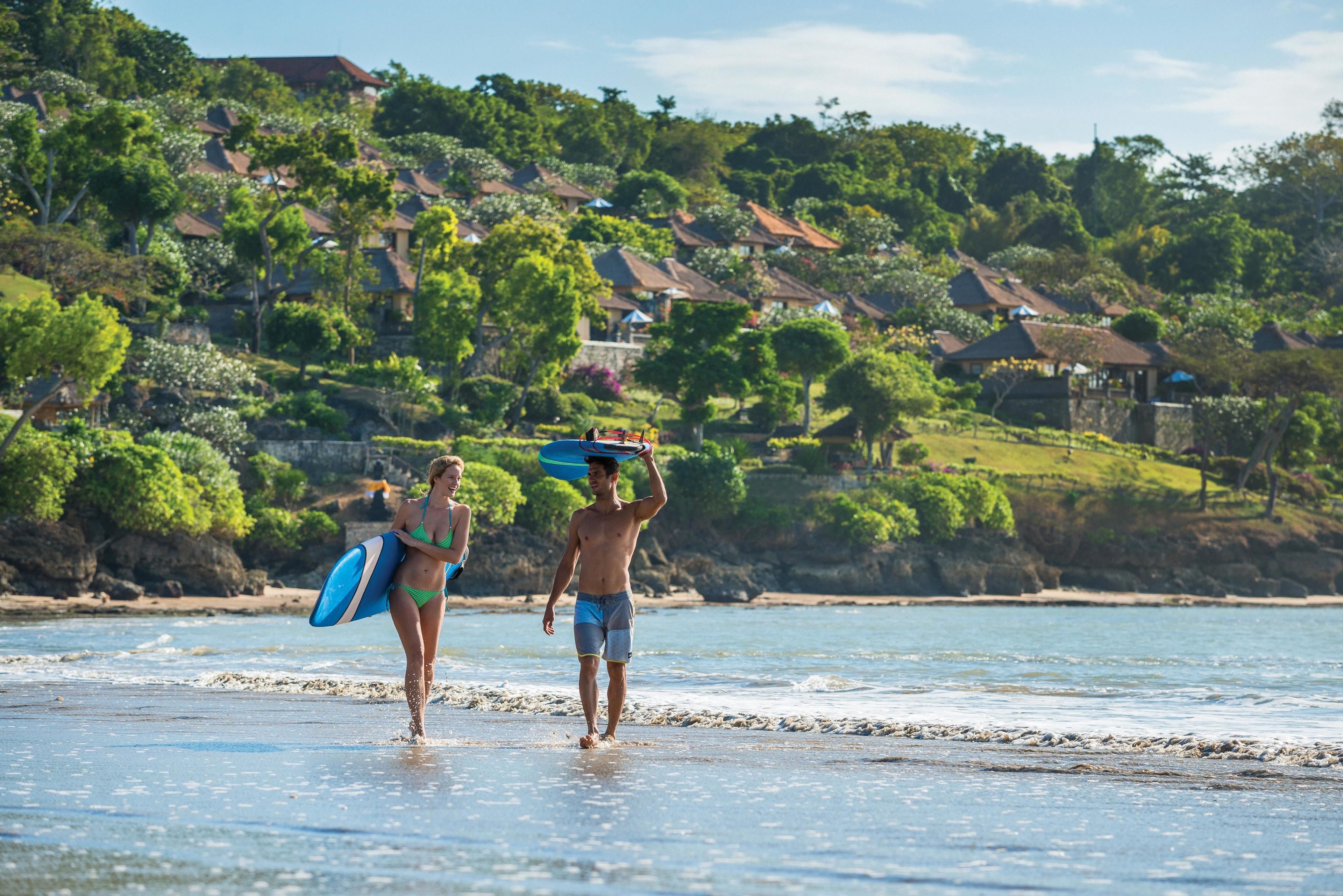 Two people walking on a beach with houses in the background.