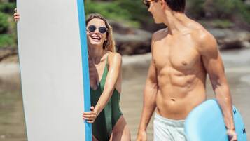 A beach scene with a person holding a surfboard and another person in a swimsuit.