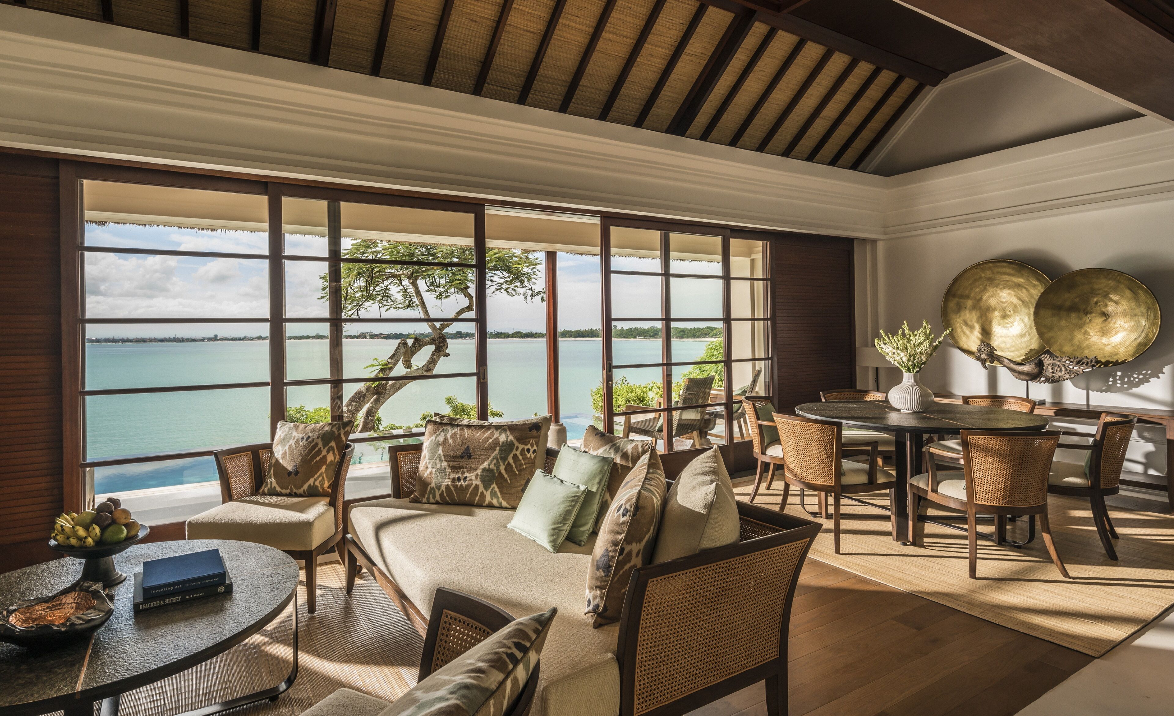 A spacious room with a large window offering a view of the sea. There is a dining area with a round table and chairs.