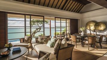 A spacious room with a large window offering a view of the sea. There is a dining area with a round table and chairs.
