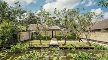 A garden with a pond, a thatched-roof structure, and a pathway.