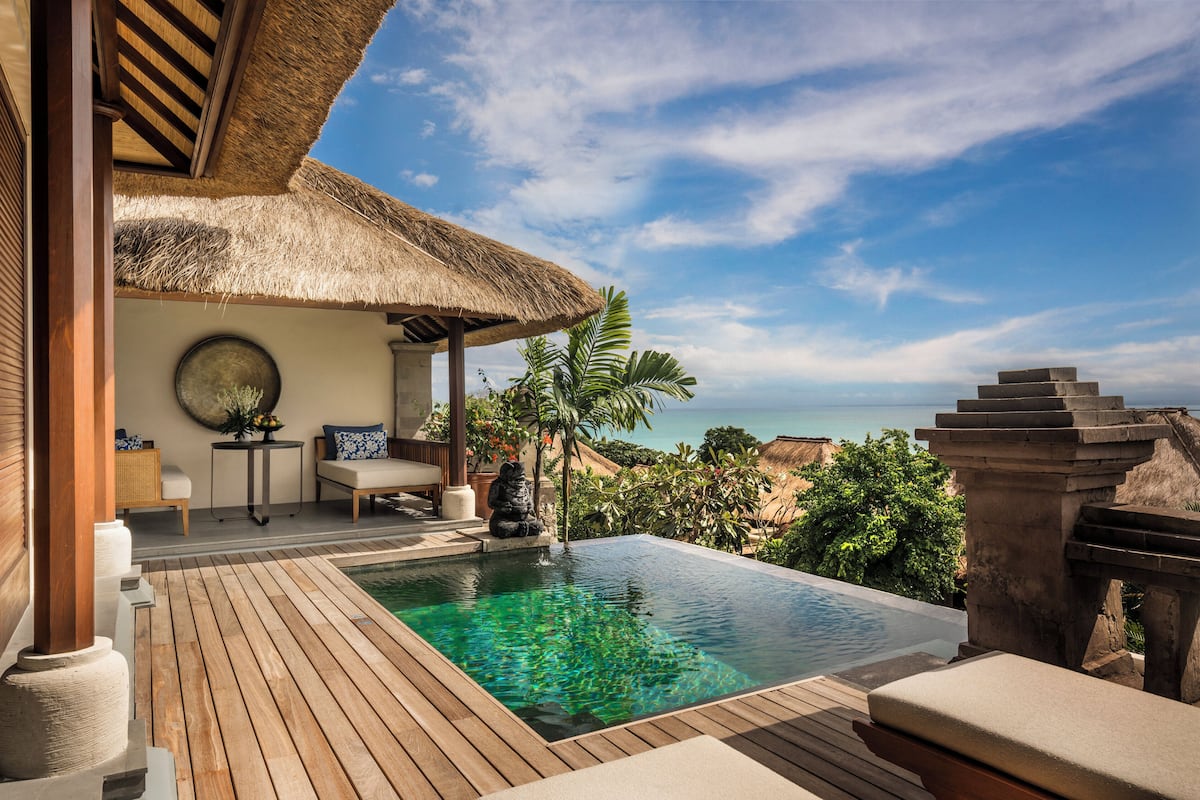 Eine Holzterrasse mit Pool, ein Gebäude mit einem Reetdach und Blick auf das Meer.