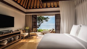 A bedroom with a large bed, a TV, a seating area with chairs, and a view of the sea. - Four Seasons Resort Bali at Jimbaran Bay (Jimbaran)