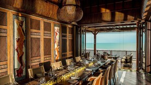 A dining area with a long table set for a meal, wooden paneling, and a view of the ocean. - Four Seasons Resort Bali at Jimbaran Bay (Jimbaran)
