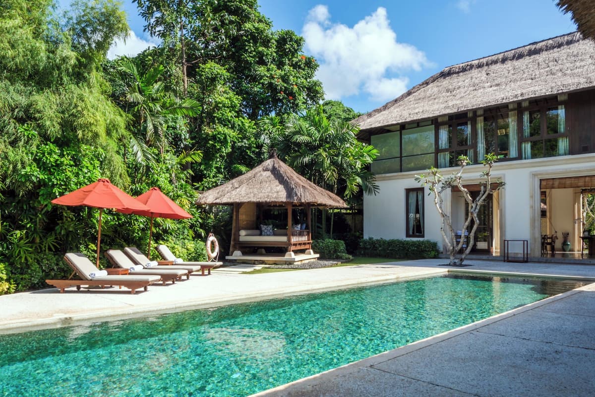 Ein Swimmingpool mit Liegestühlen und einem Gazebo mit Reetdach.