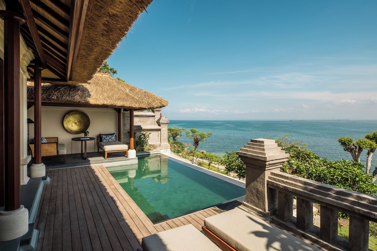 Ein privater Poolbereich mit einem Reetdach, einer Holzterrasse und Blick aufs Meer.