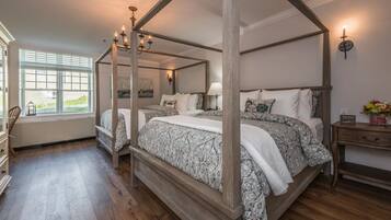 A four-poster canopy bed with a nightstand and a lamp, a dresser, and a window with blinds.