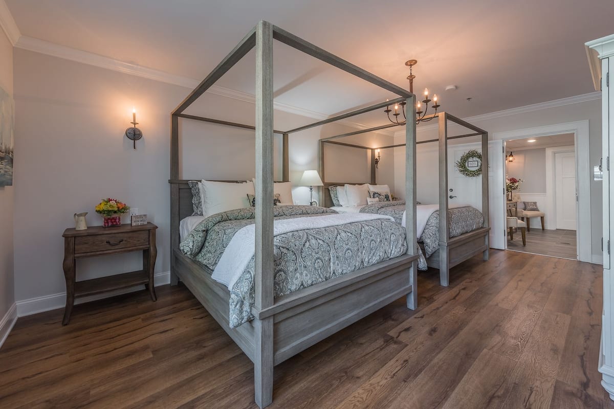 A four-poster canopy bed with a wooden frame, a nightstand with a lamp, and a small table with a vase of flowers.
