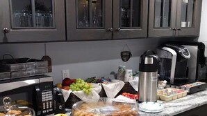 A kitchen with a coffee maker, a fruit bowl, and a bread display.
