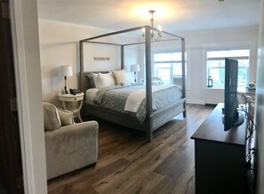 A four-poster bed with a canopy, a bedside table with a lamp, a chair, and a television on a stand.