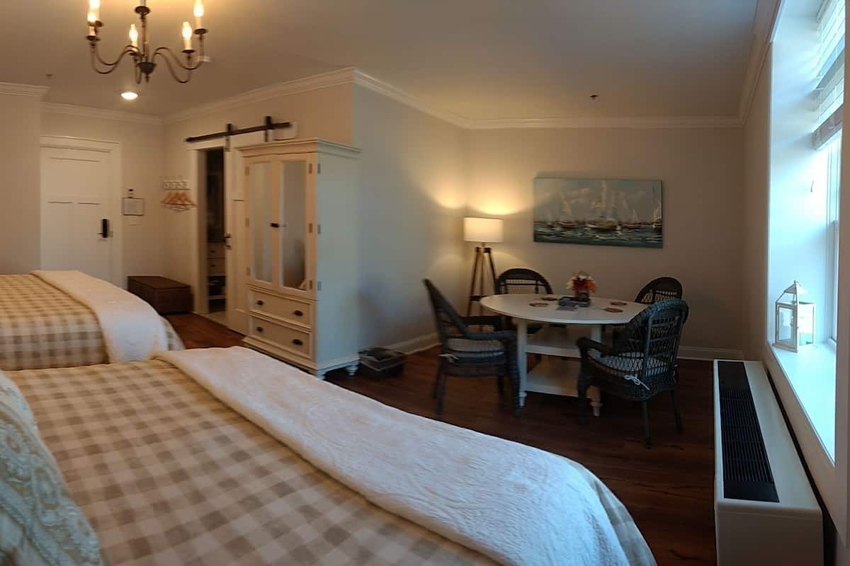 A hotel room with two beds, a dining area, a mirror, and a painting on the wall.
