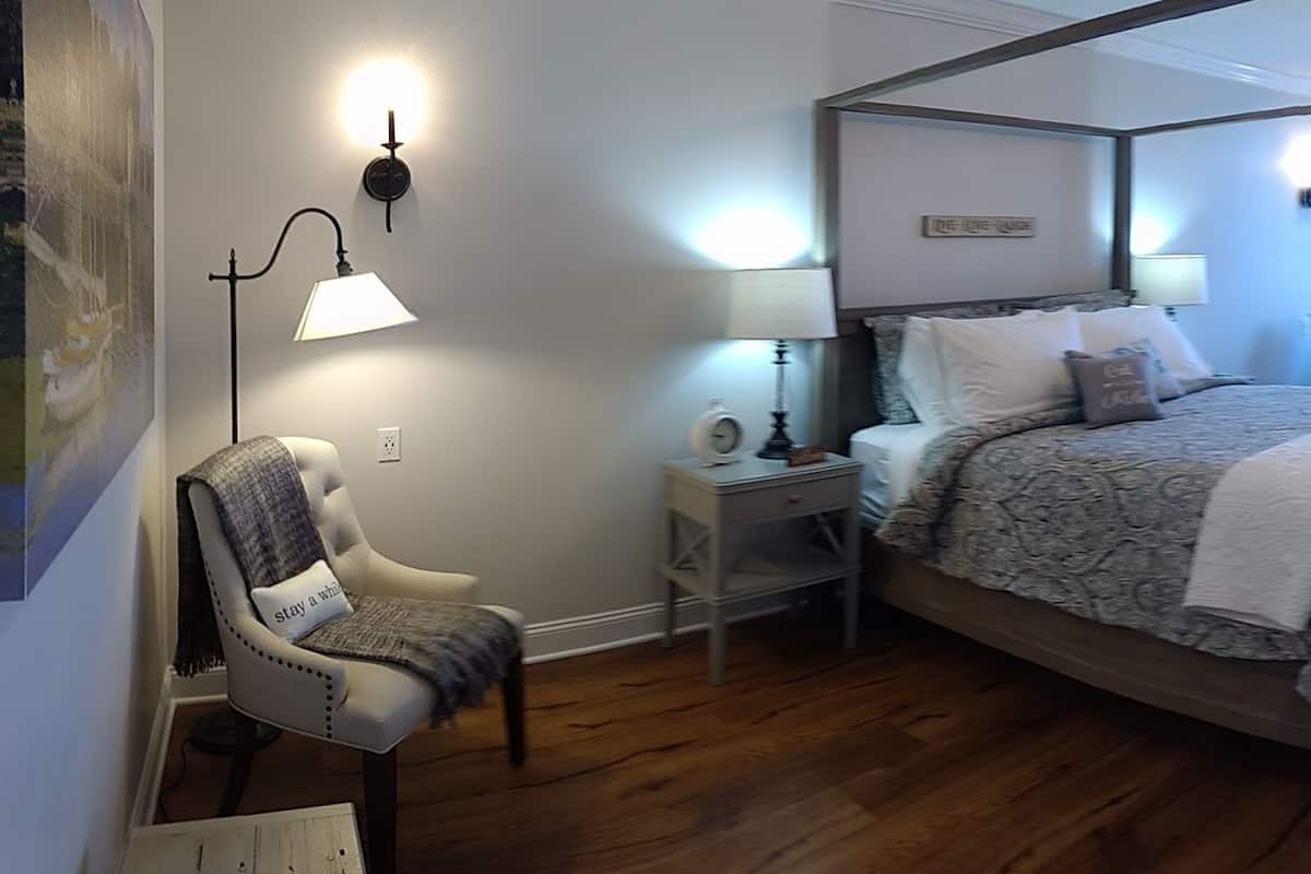 A four-poster bed with a canopy, a bedside table with a lamp, a chair with a cushion, and a bench.