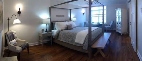 A four-poster bed with a canopy, a bedside table with a lamp, a chair with a cushion, and a bench.